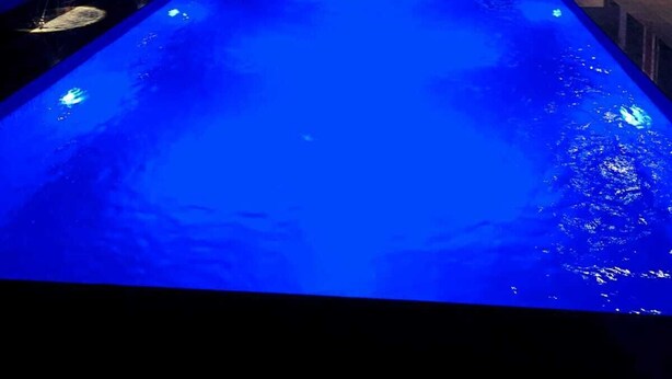 Une piscine dotée d’un élément décoratif aquatique illuminé de lumière bleue, entourée d’un bâtiment avec de grandes fenêtres et un balcon.