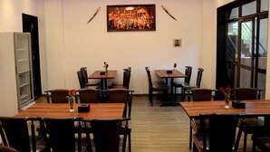 Un coin repas comprenant deux tables et des chaises, un ventilateur de plafond, un tableau accroché au mur et une fenêtre donnant sur un paysage.