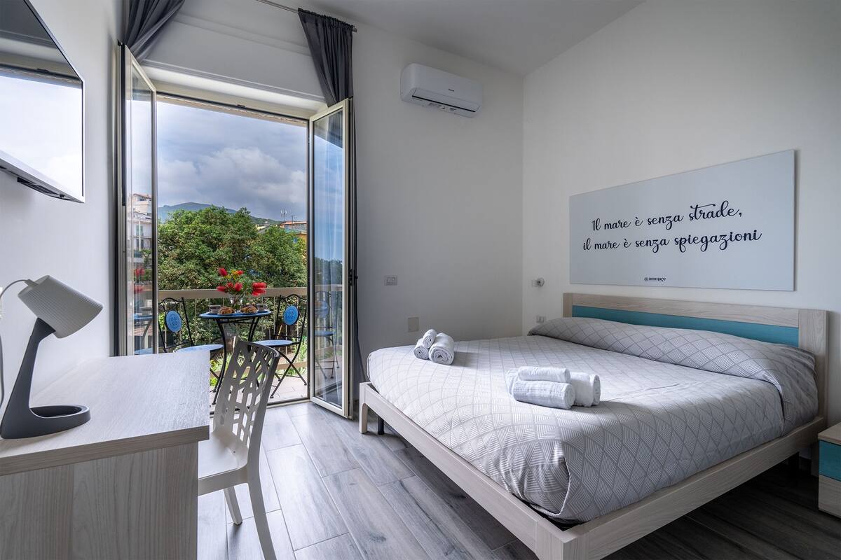 A modern bedroom with a bed, a desk, and a balcony with a view of the city.
