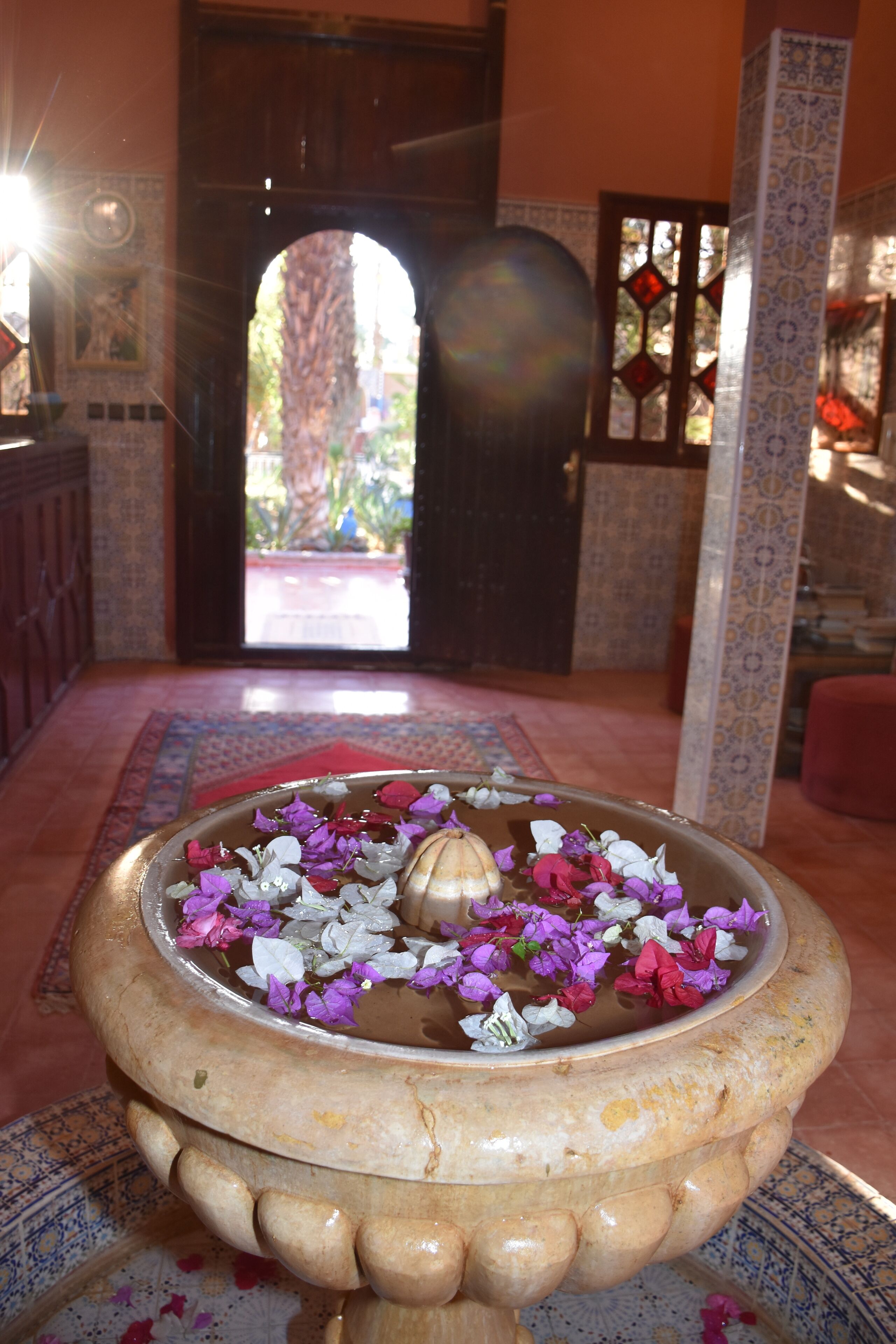A traditional water fountain with flowers in a room with patterned tiles and a wooden door.
