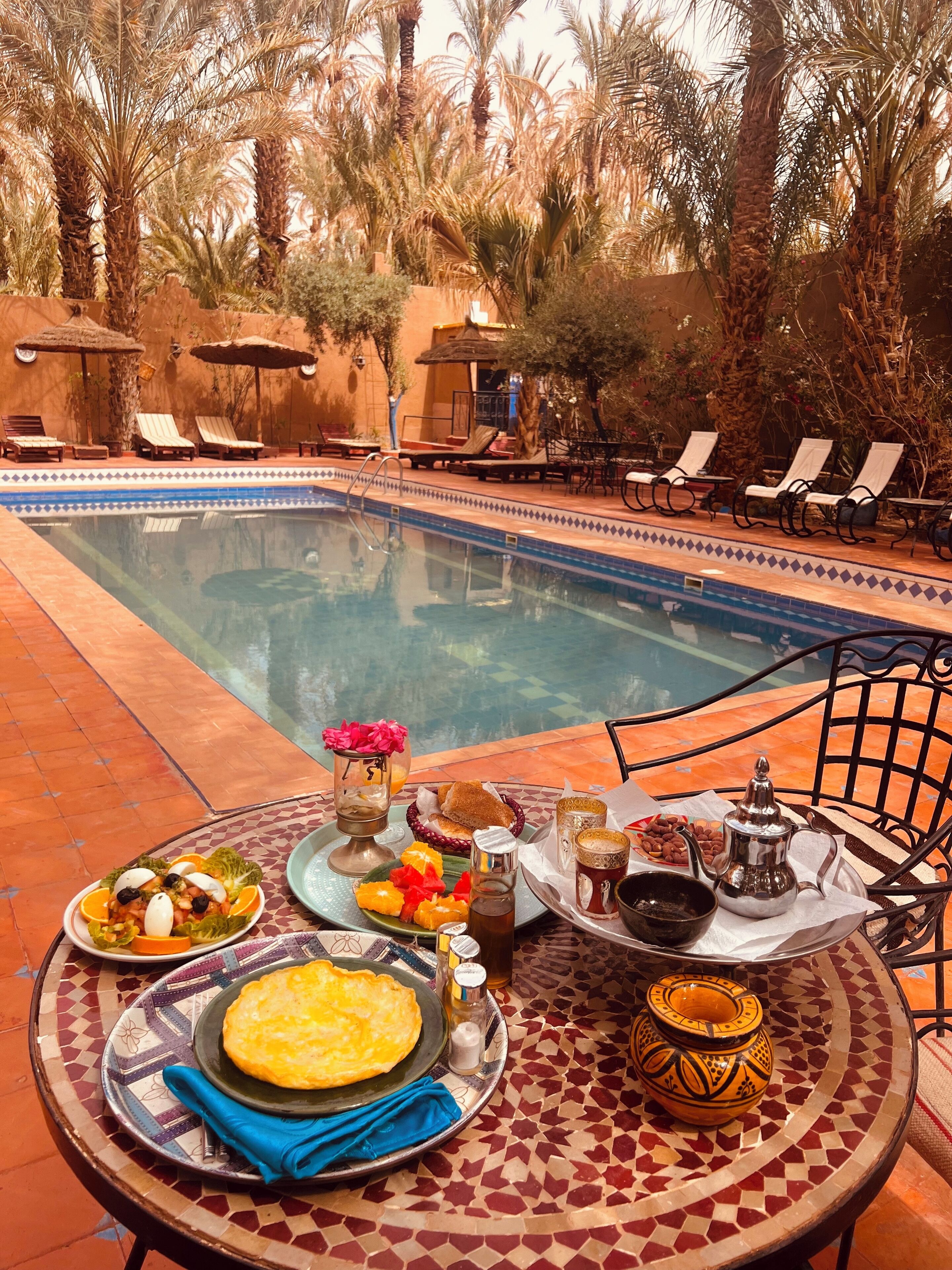 A poolside dining area with a table set for breakfast, including plates of food, a teapot, and a pitcher.