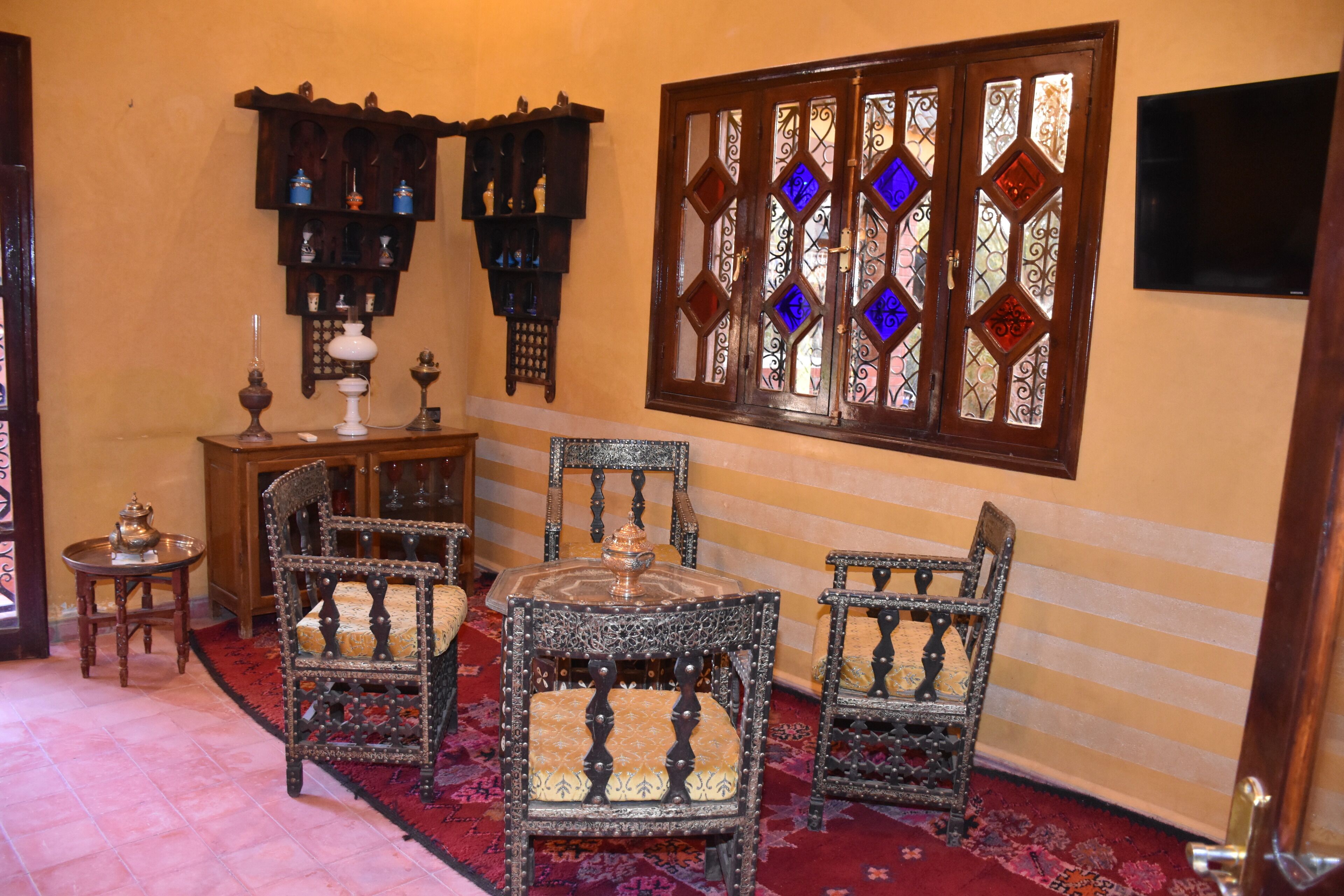 A room with ornate wooden furniture, a patterned rug, and a stained glass window.