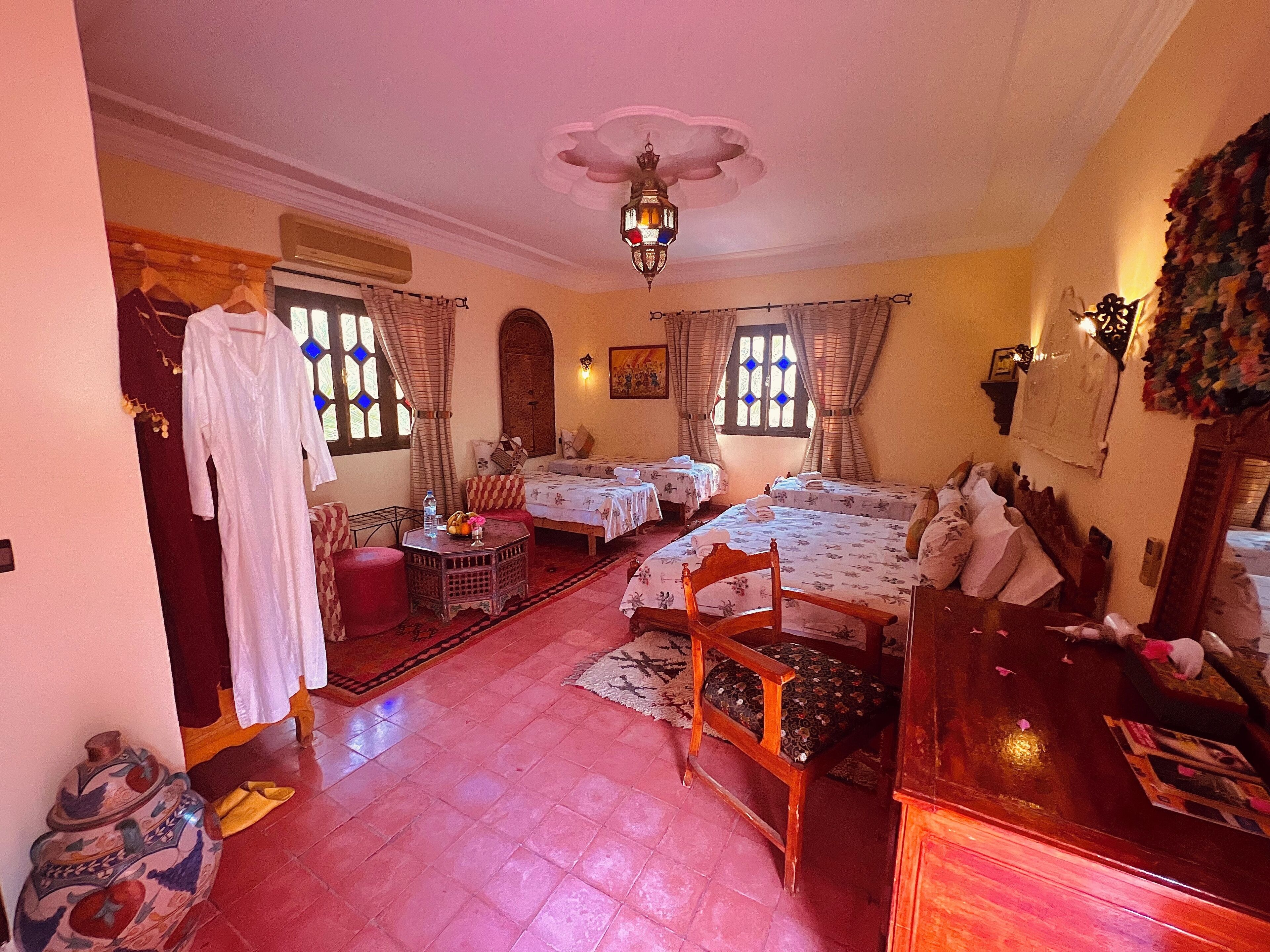 Une chambre traditionnelle avec deux lits, une chaise en bois, une petite table et une lampe décorative.