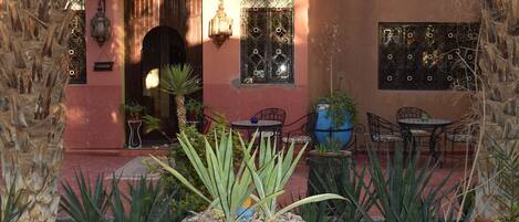 Un patio con una fuente central, rodeado de plantas en macetas y mobiliario exterior.
