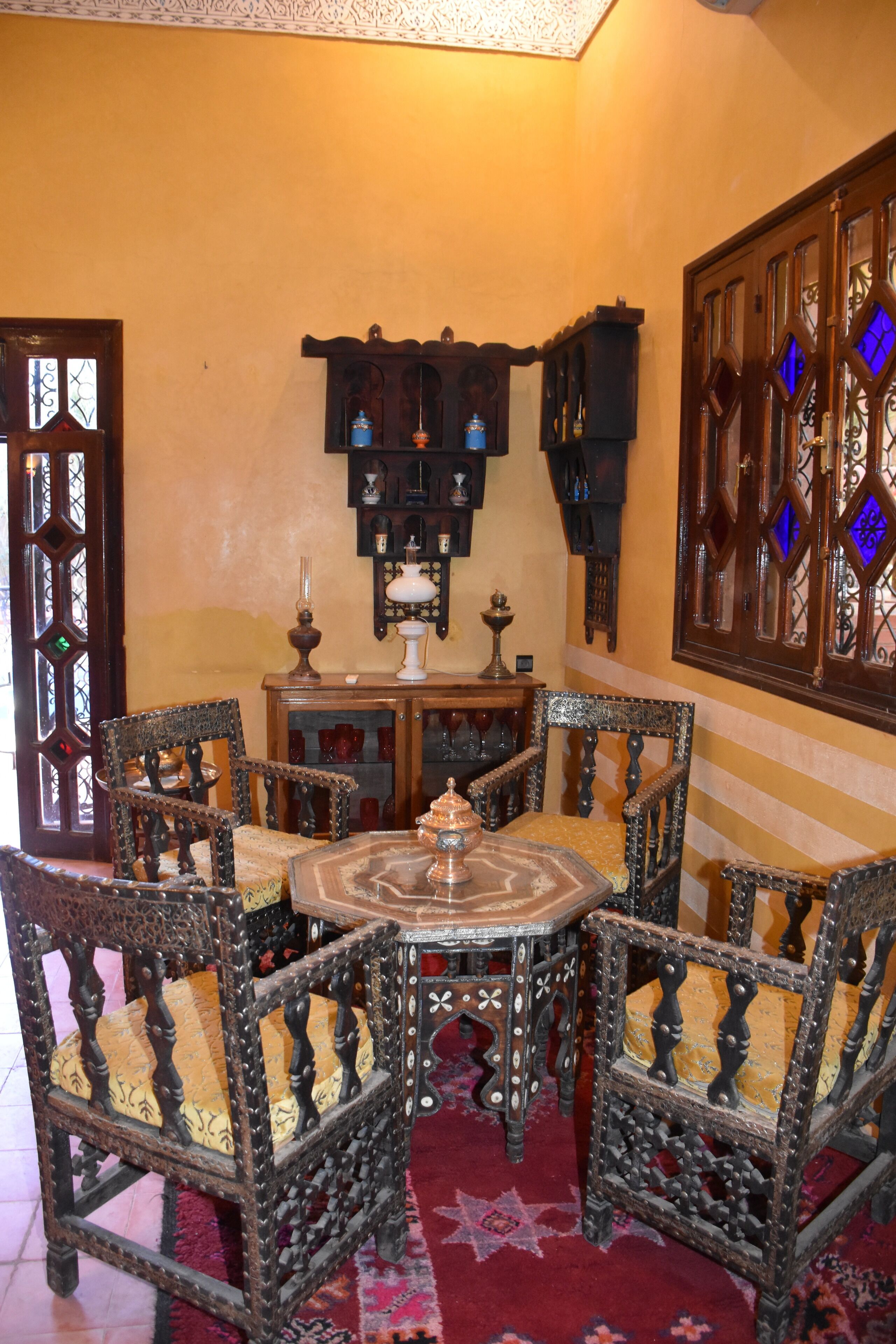Un intérieur marocain traditionnel, avec des meubles en bois richement décorés, un tapis à motifs et un panneau mural ornemental.