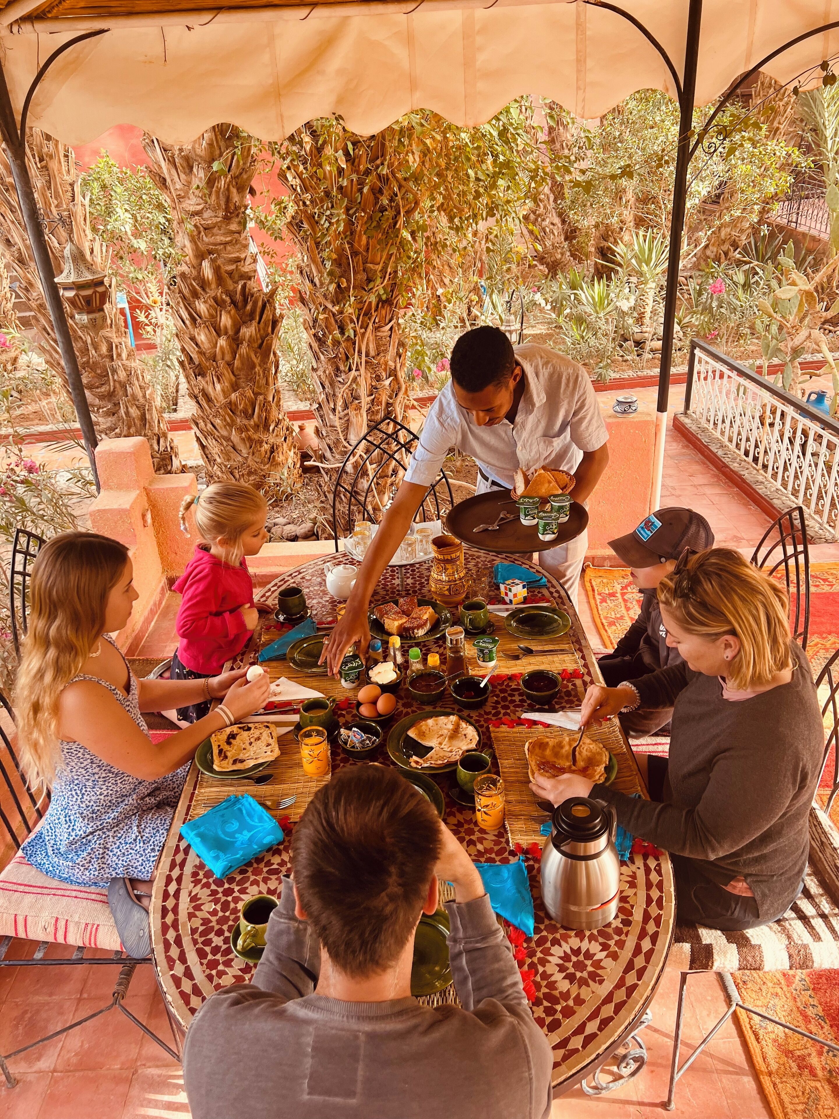 Un grupo de personas cenando en una mesa al aire libre, con diversos platos y bebidas.