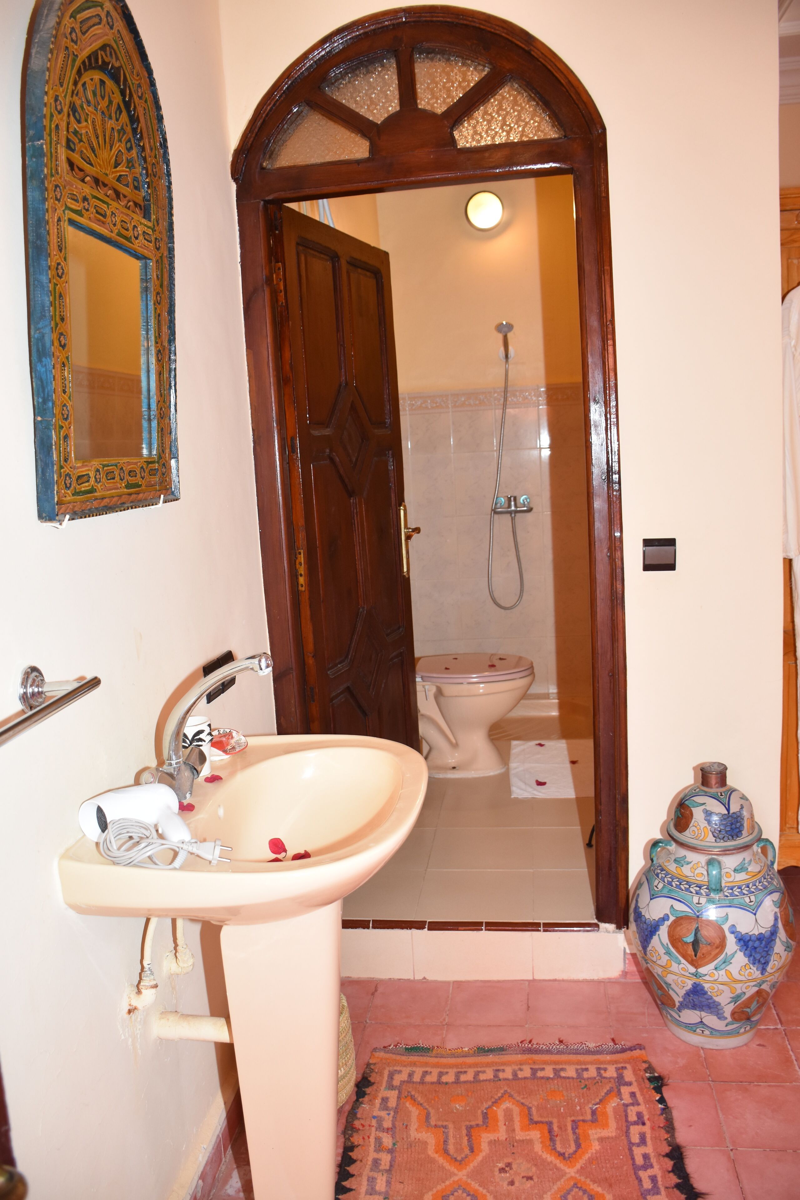 Un baño con lavamanos, espejo, ducha, inodoro y un jarrón decorativo.