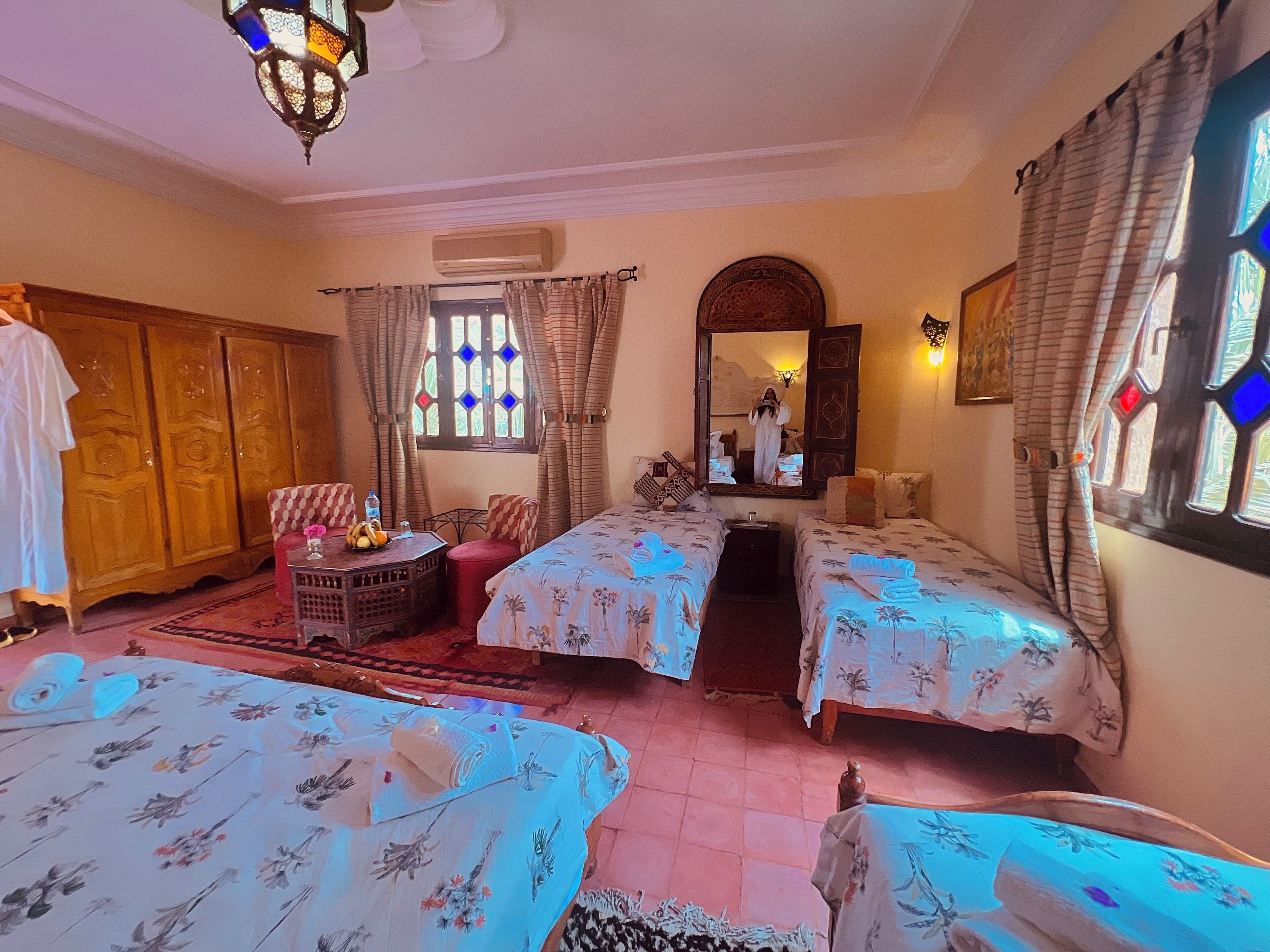 A hotel room with two beds, a wooden wardrobe, a small table with a water bottle, and a mirror.