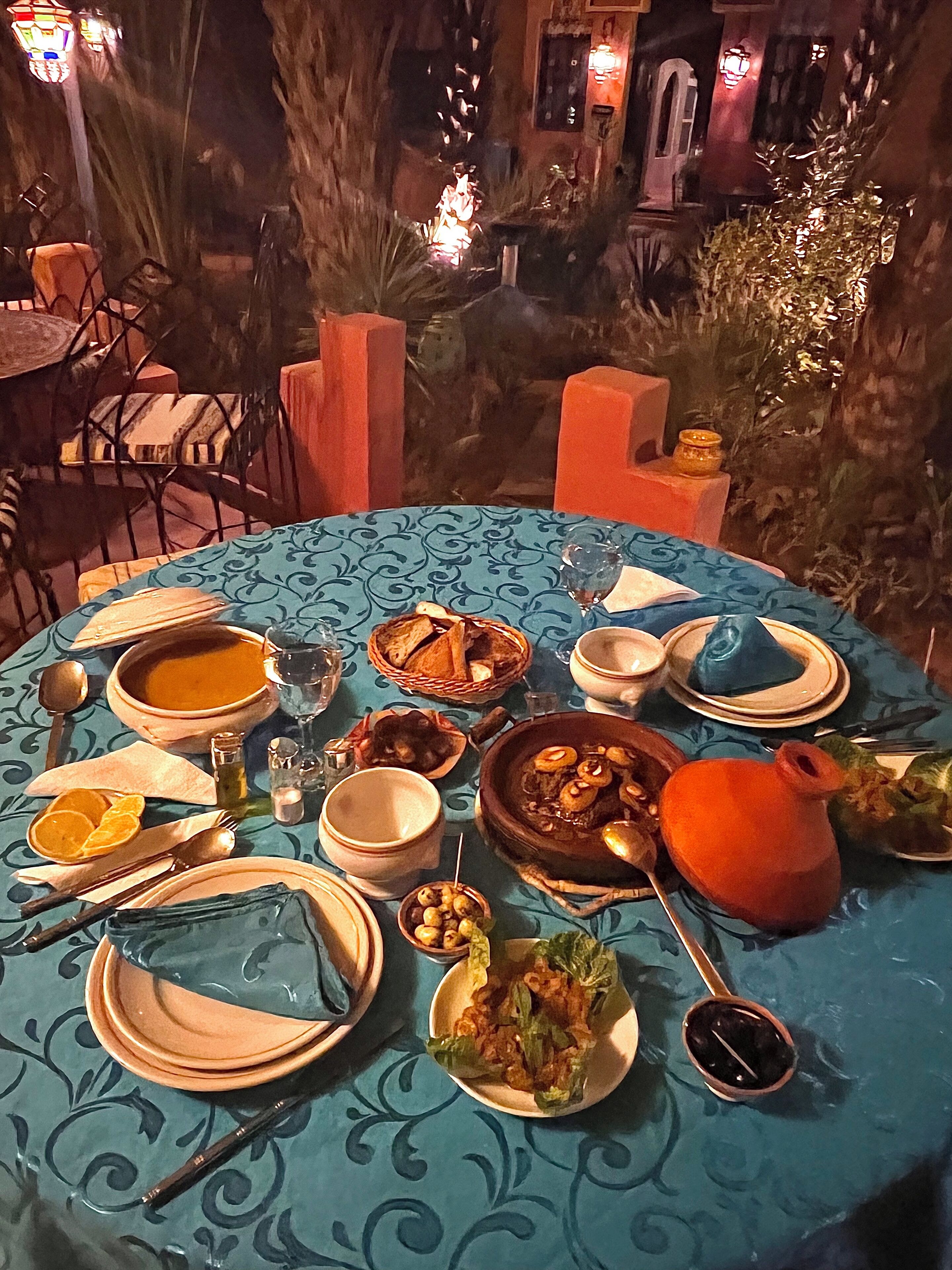 A table set with various dishes, including soup and salad, in an outdoor dining area with a blue tablecloth and rustic decor.