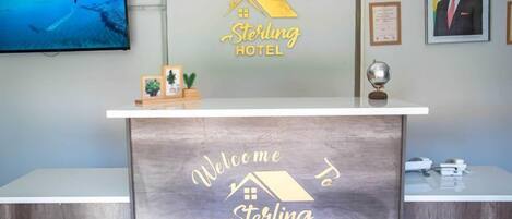 Una recepción de hotel con un letrero que dice "Sterling Hotel", un televisor, certificados enmarcados y un globo terráqueo.