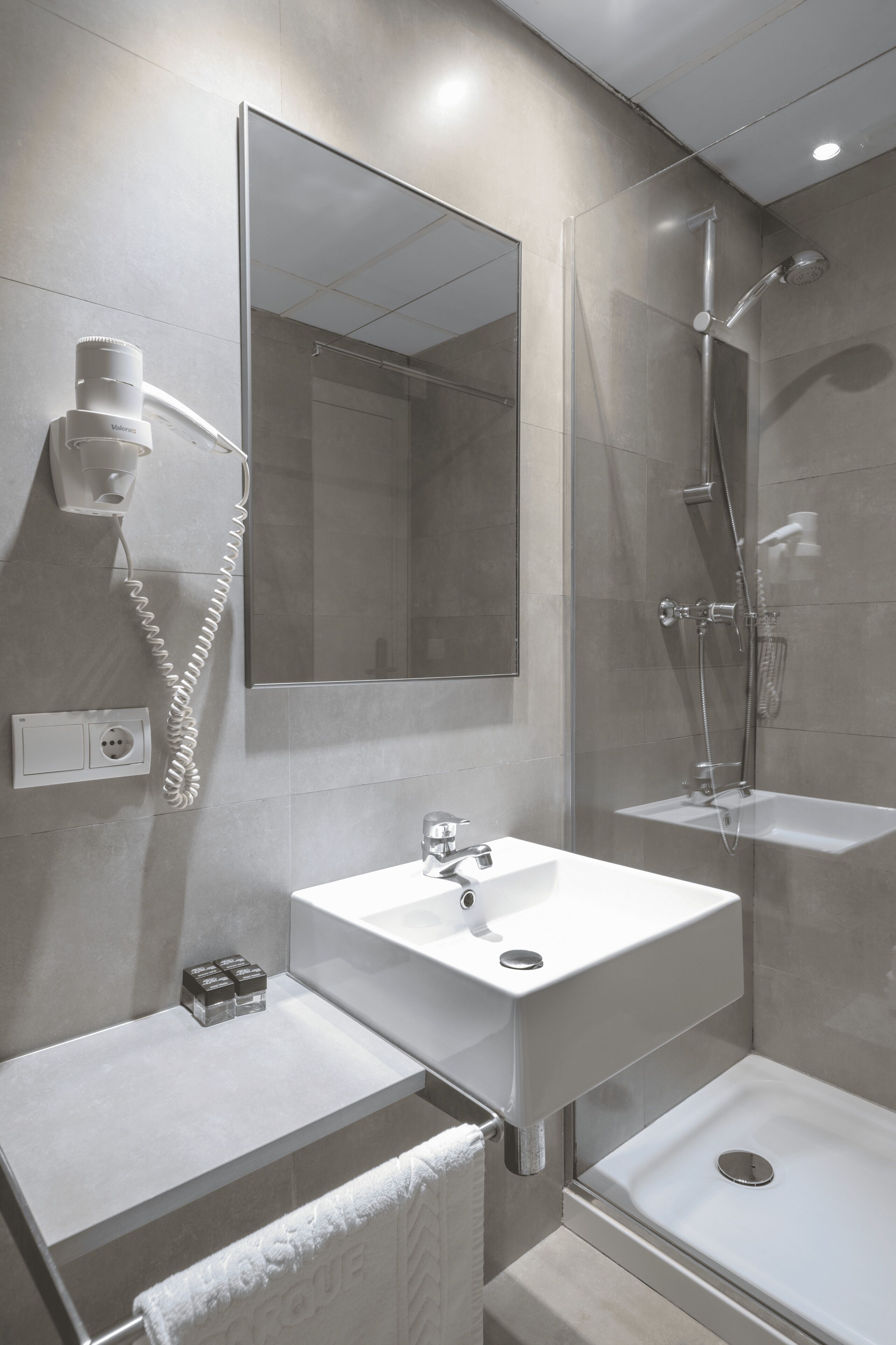 A modern bathroom with a large mirror, a sink, a shower, and a hairdryer mounted on the wall.