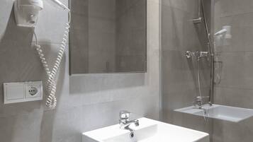 Uma casa de banho moderna com um espelho grande, uma pia, um chuveiro e um secador de cabelo fixado na parede.