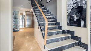 A staircase with marble steps and a wooden handrail, leading to a room with a glass display case and a framed picture on the wall.