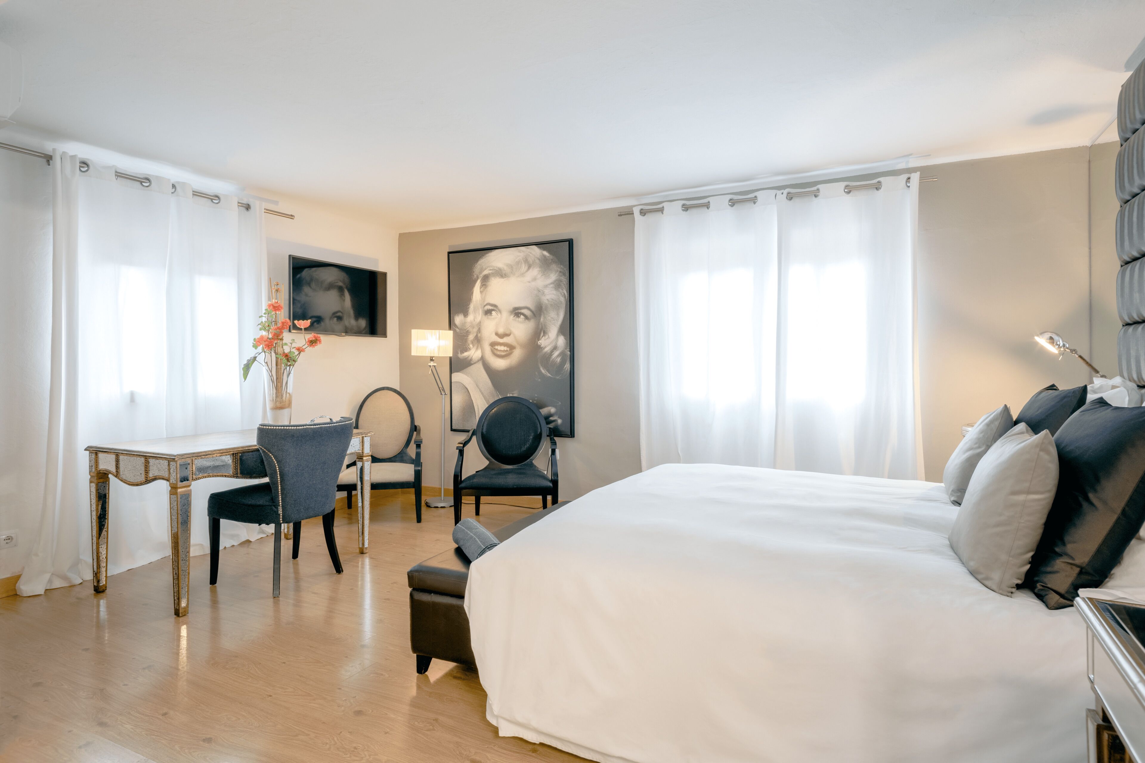 Habitación de hotel con una cama grande, un escritorio, dos sillas y un televisor montado en la pared.