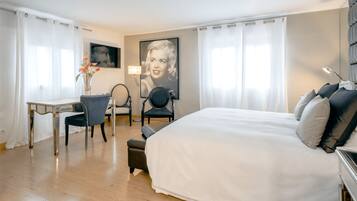 Habitación de hotel con una cama grande, un escritorio, dos sillas y un televisor montado en la pared.