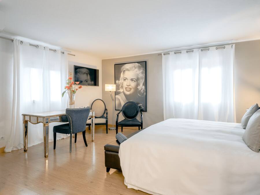 Habitación de hotel con una cama grande, un escritorio, dos sillas y un televisor montado en la pared.