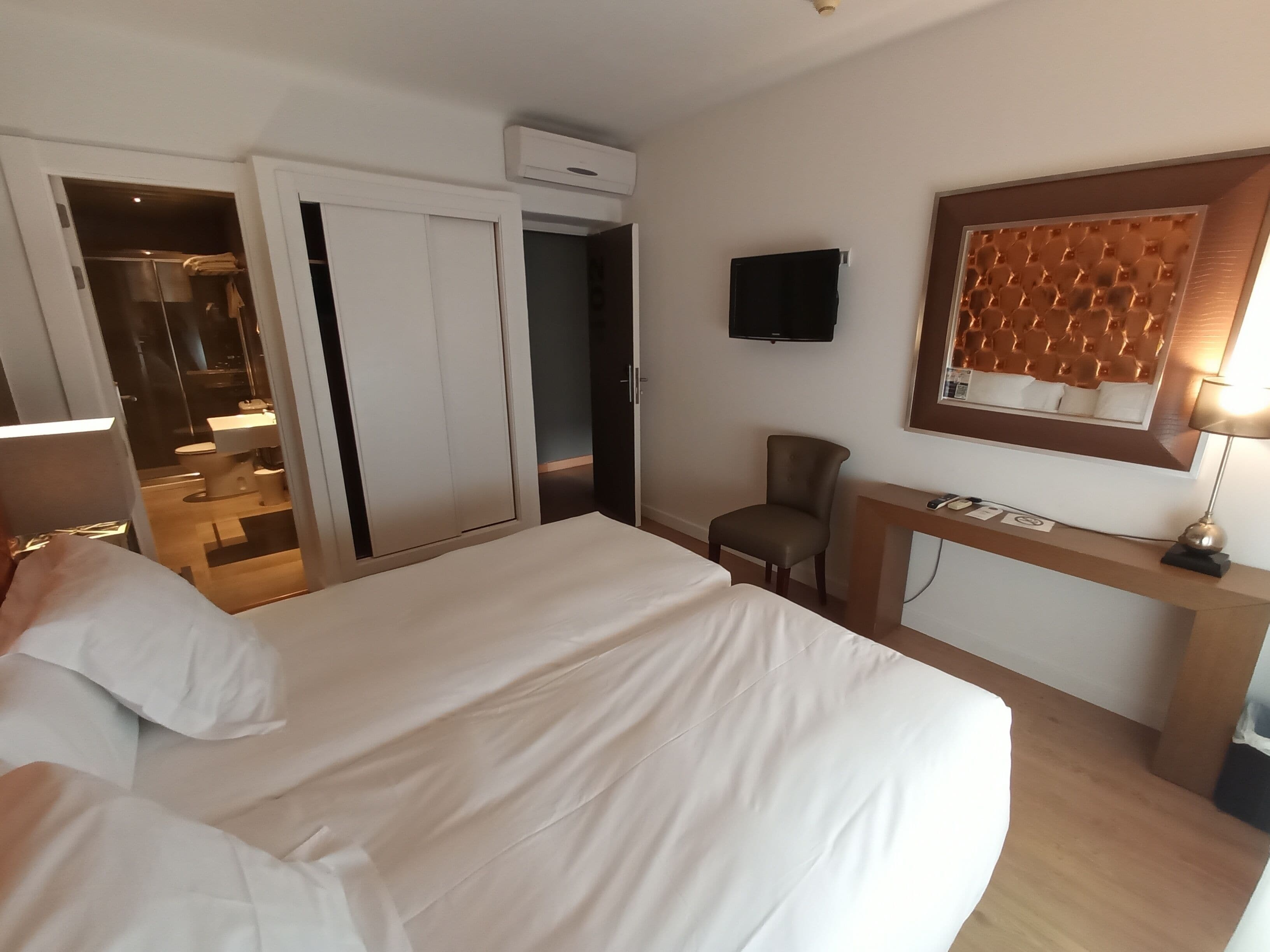 Ein Hotelzimmer mit einem großen Bett, einem Schreibtisch mit Stuhl, einem Fernseher und einem durch eine offene Tür einsehbaren Badezimmer.