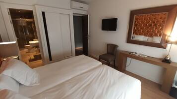 Ein Hotelzimmer mit einem großen Bett, einem Schreibtisch mit Stuhl, einem Fernseher und einem durch eine offene Tür einsehbaren Badezimmer.