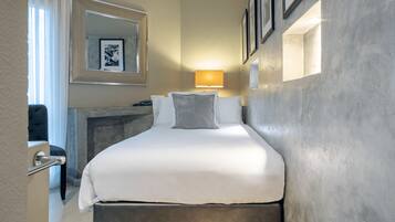 Une chambre d’hôtel avec un lit, une table de chevet, une lampe, un miroir et un tableau encadré au mur.