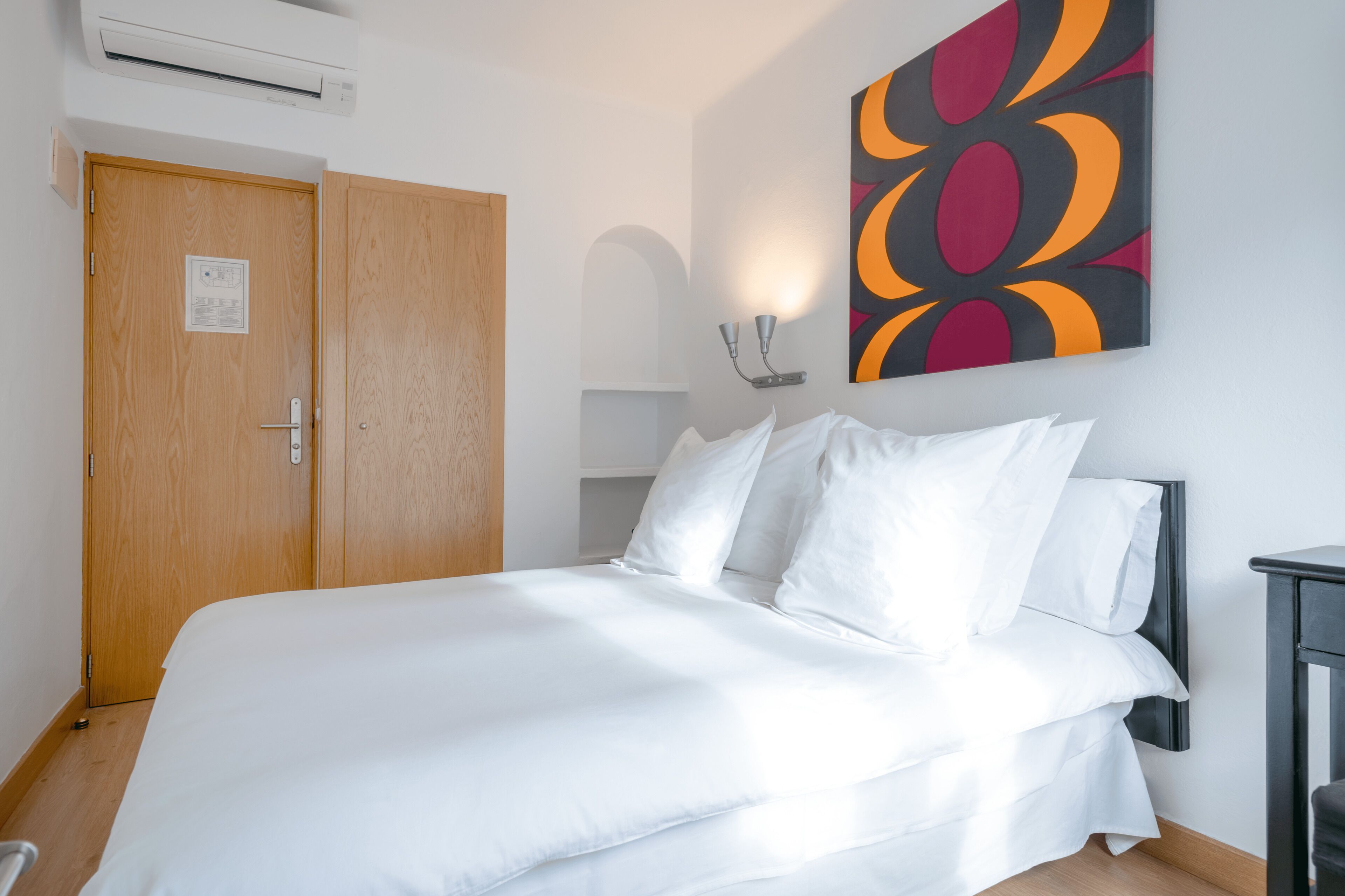Una cama bien tendida en una habitación de hotel, con una puerta de madera y una obra de arte colgada en la pared.