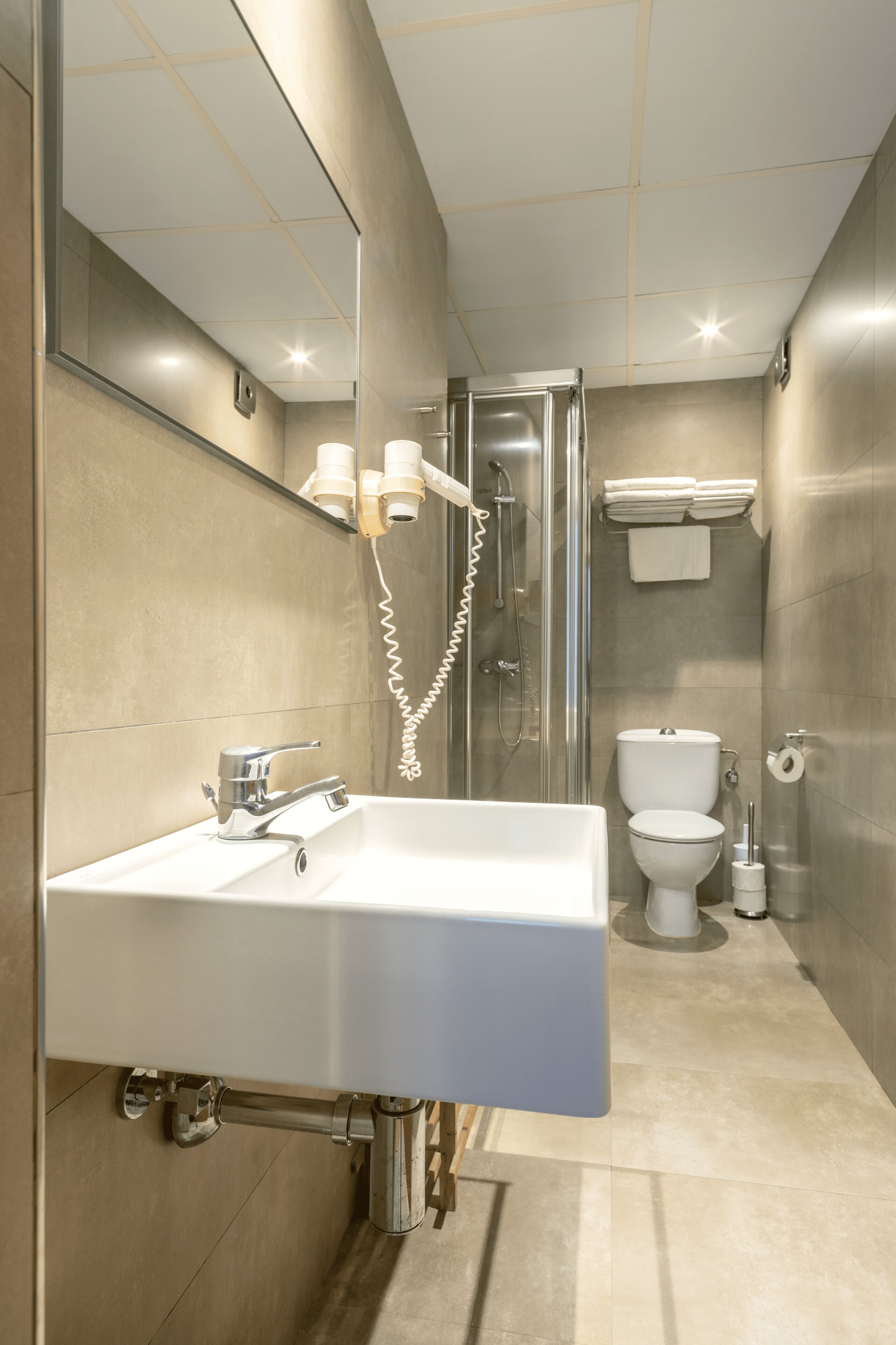 A modern bathroom with a large mirror, a sink, a shower, and a toilet.