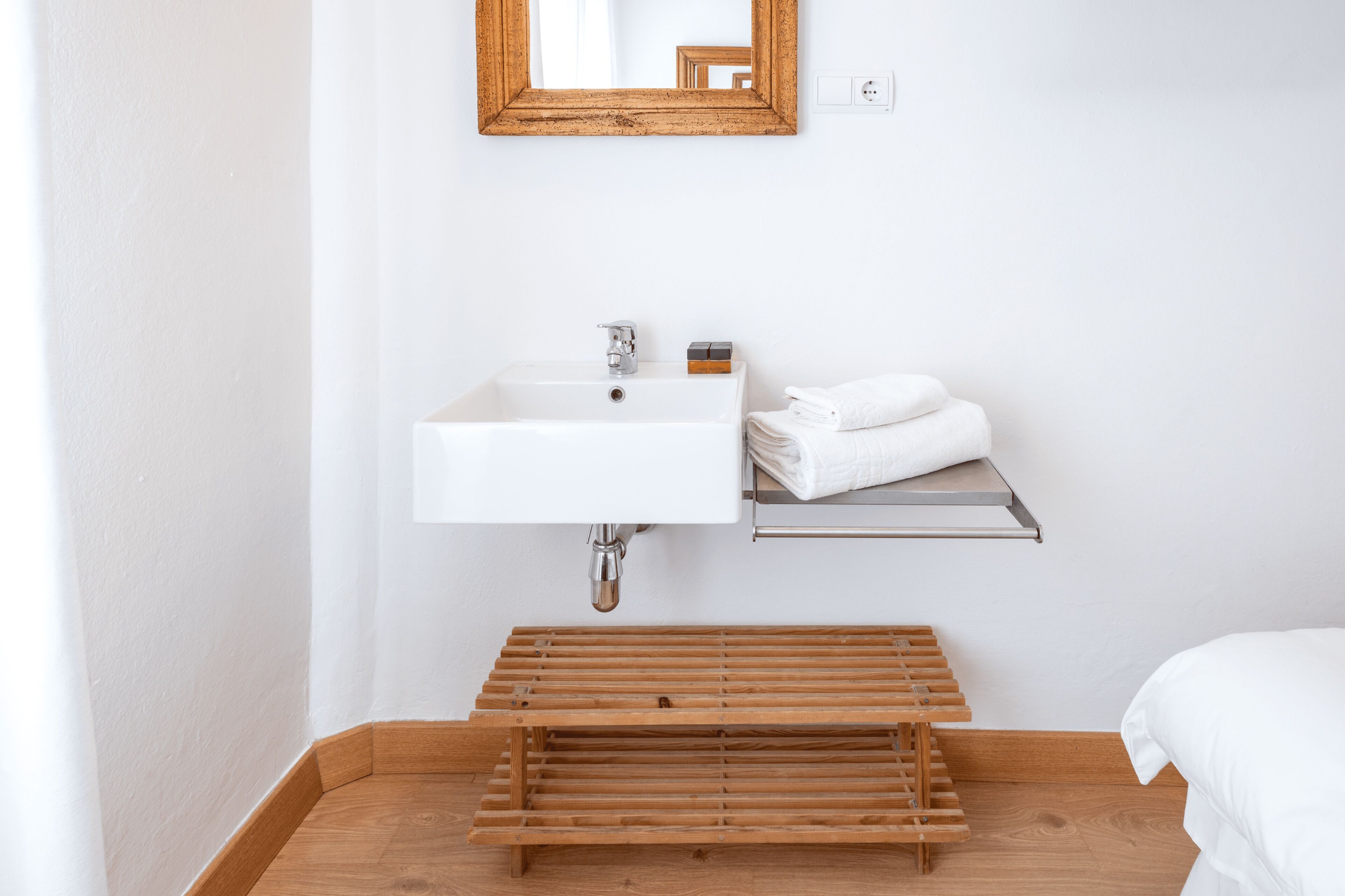 A bathroom with a white sink, a wooden shelf with towels, and a wooden bench.