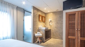 A hotel room with a large bed, a bathroom with a sink and mirror, and a wooden wardrobe.