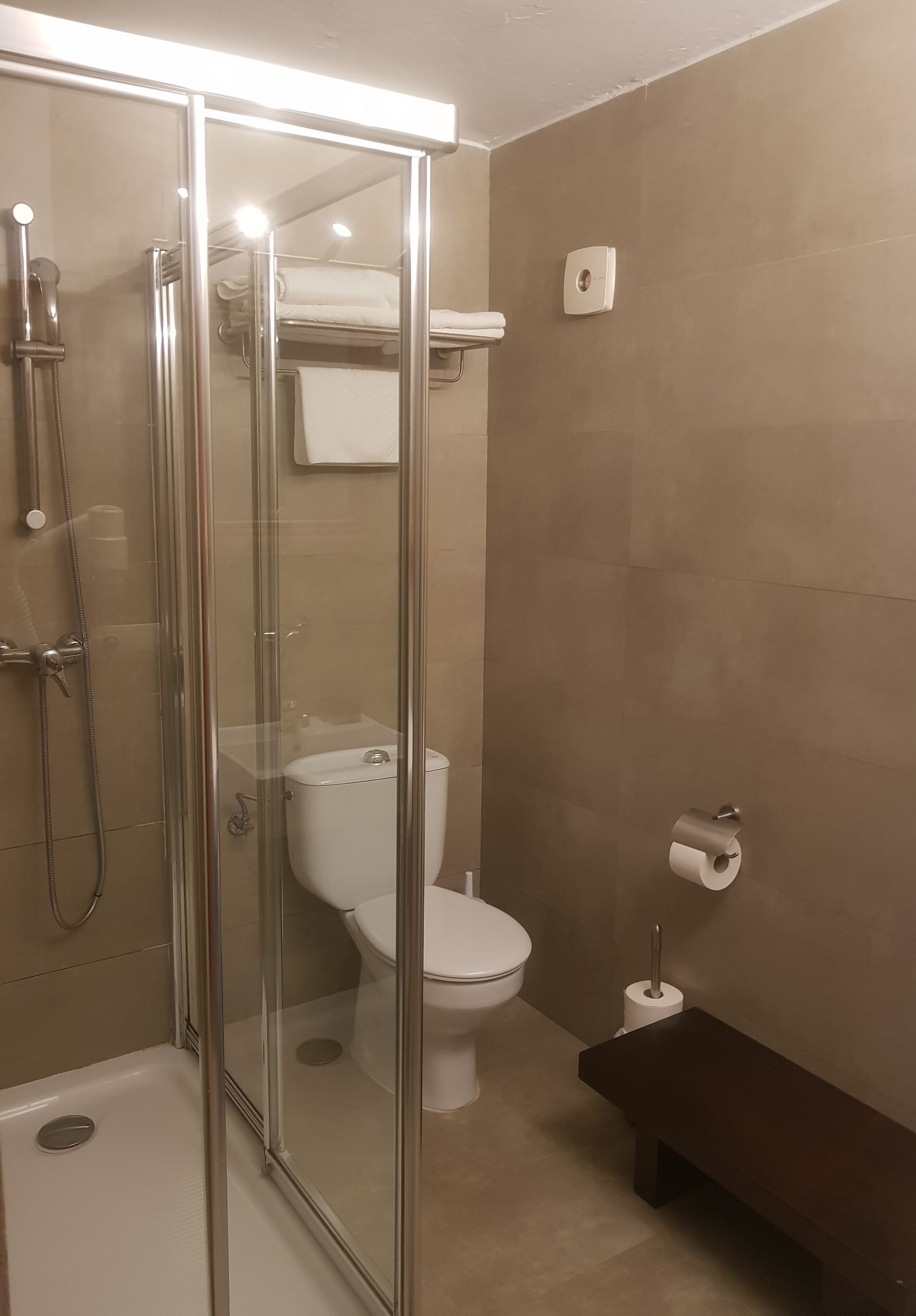 Moderni kylpyhuone, jossa on lasiseinällä varustettu suihku, wc ja penkki.