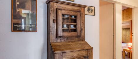 A wooden cabinet with glass doors, a framed picture above it, and a small chair beside it.