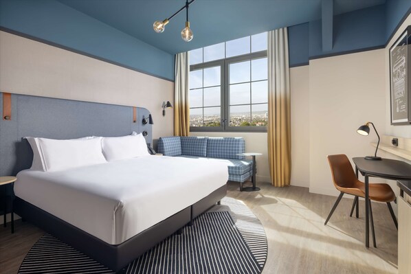 A modern hotel room with a large bed, a seating area, a desk, and a window with a city view. - Hyatt Place Rouen (Rouen)
