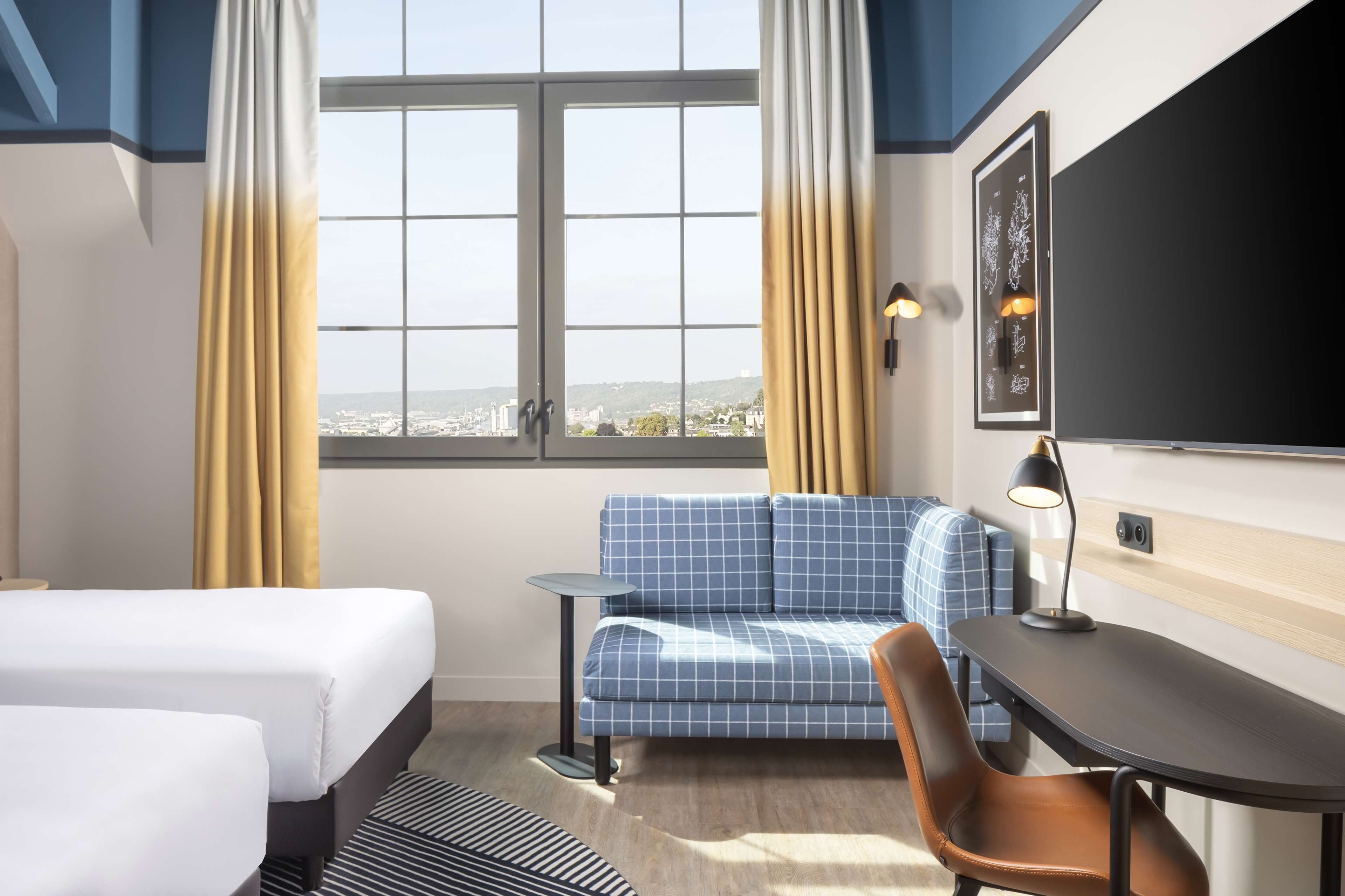 Habitación de hotel con dos camas, un sofá, un escritorio y vista a la ciudad.