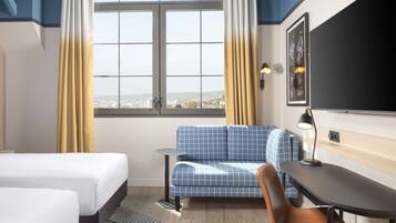Habitación de hotel con dos camas, un sofá, un escritorio y vista a la ciudad.