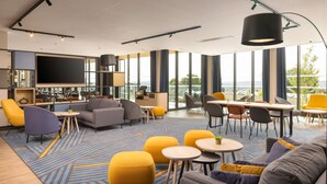 A modern hotel lobby with a large TV, comfortable seating, a bar area, and large windows offering a view. - Hyatt Place Rouen (Rouen)