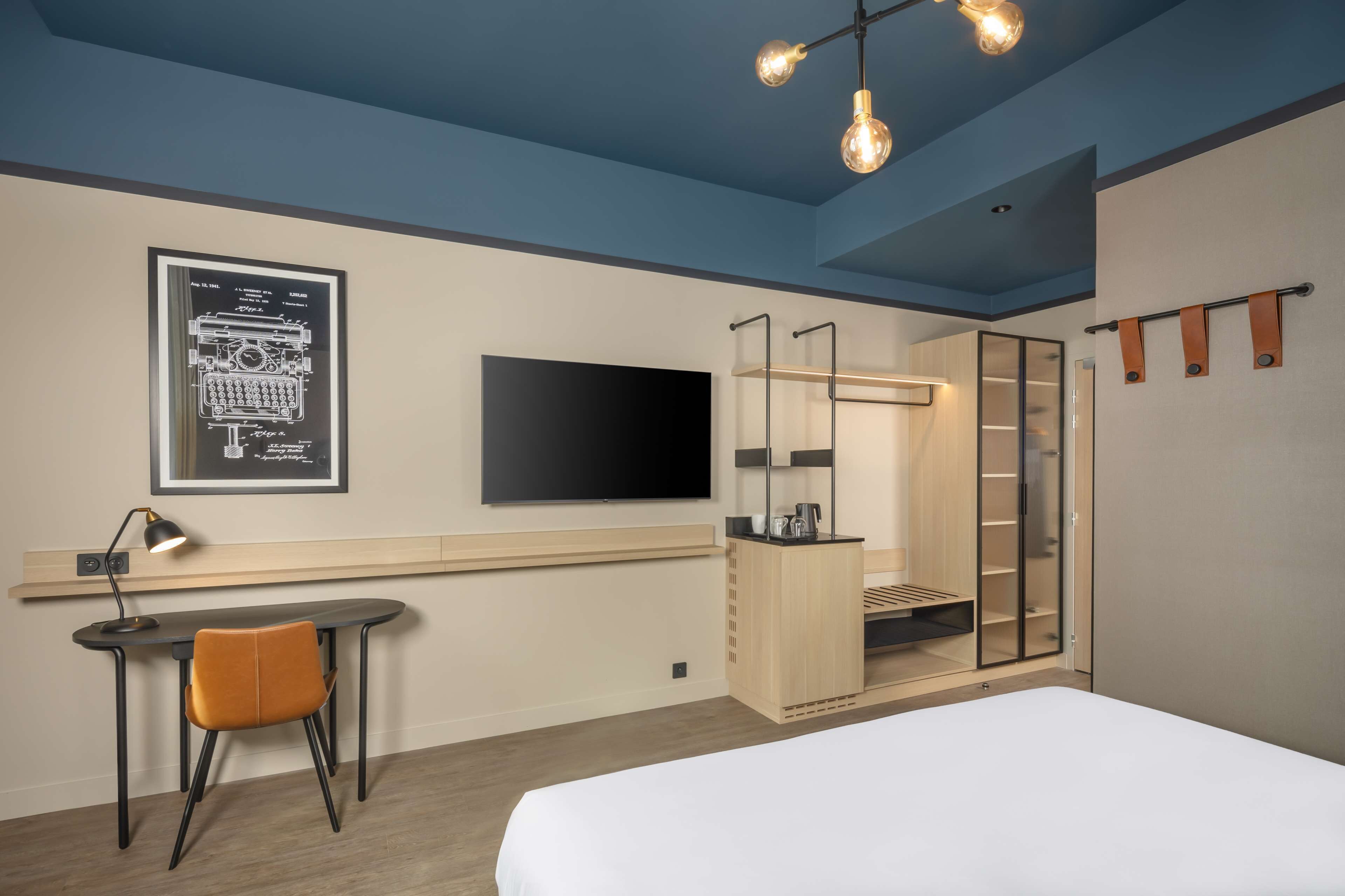 Una habitación de hotel moderna con escritorio, silla, cama, armario y televisor montado en la pared.