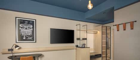 A modern hotel room with a desk, chair, bed, wardrobe, and a TV mounted on the wall.