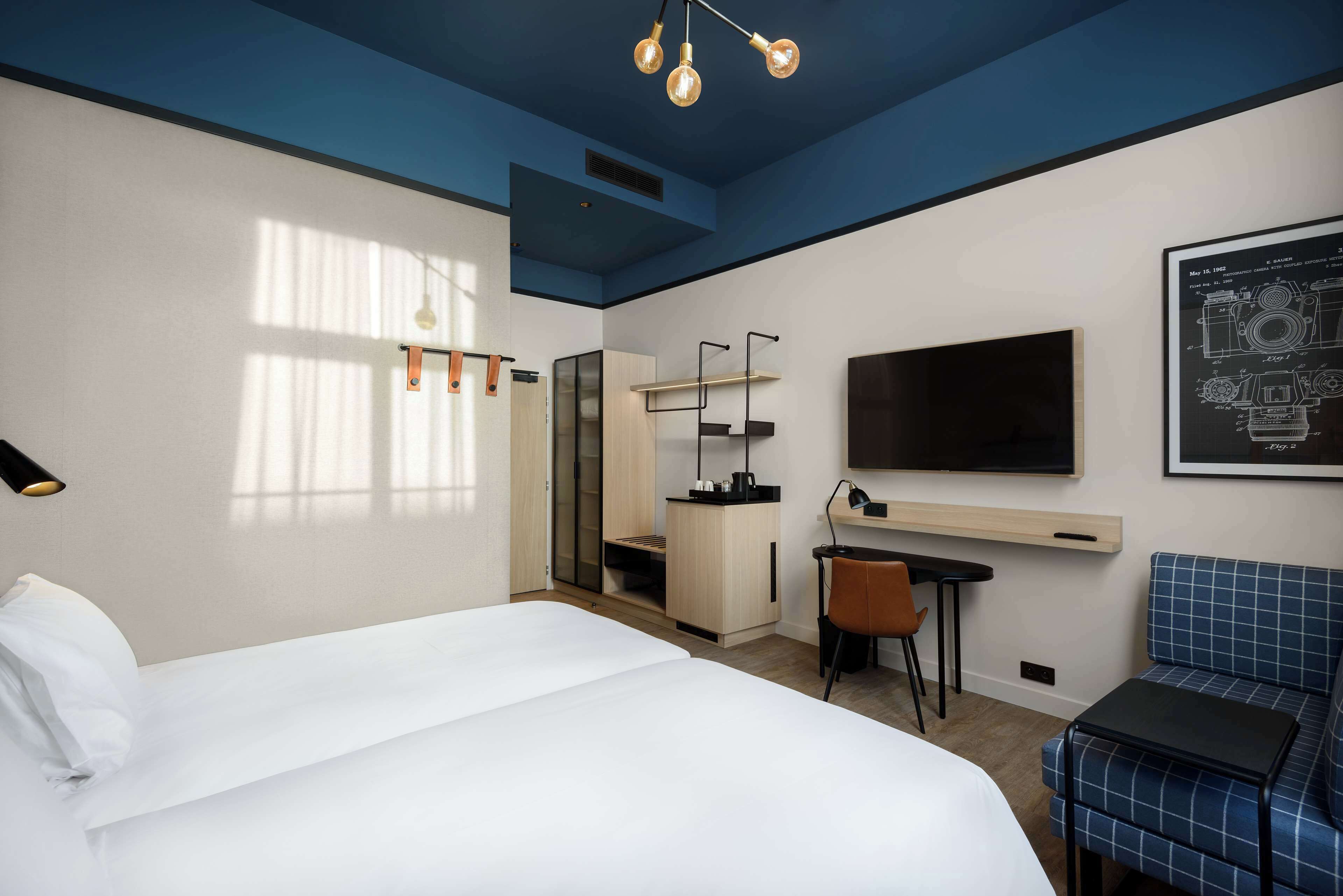 A modern hotel room with a large bed, a desk, a chair, a TV, and a blue sofa.