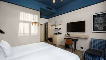 A modern hotel room with a large bed, a desk, a chair, a TV, and a blue sofa.