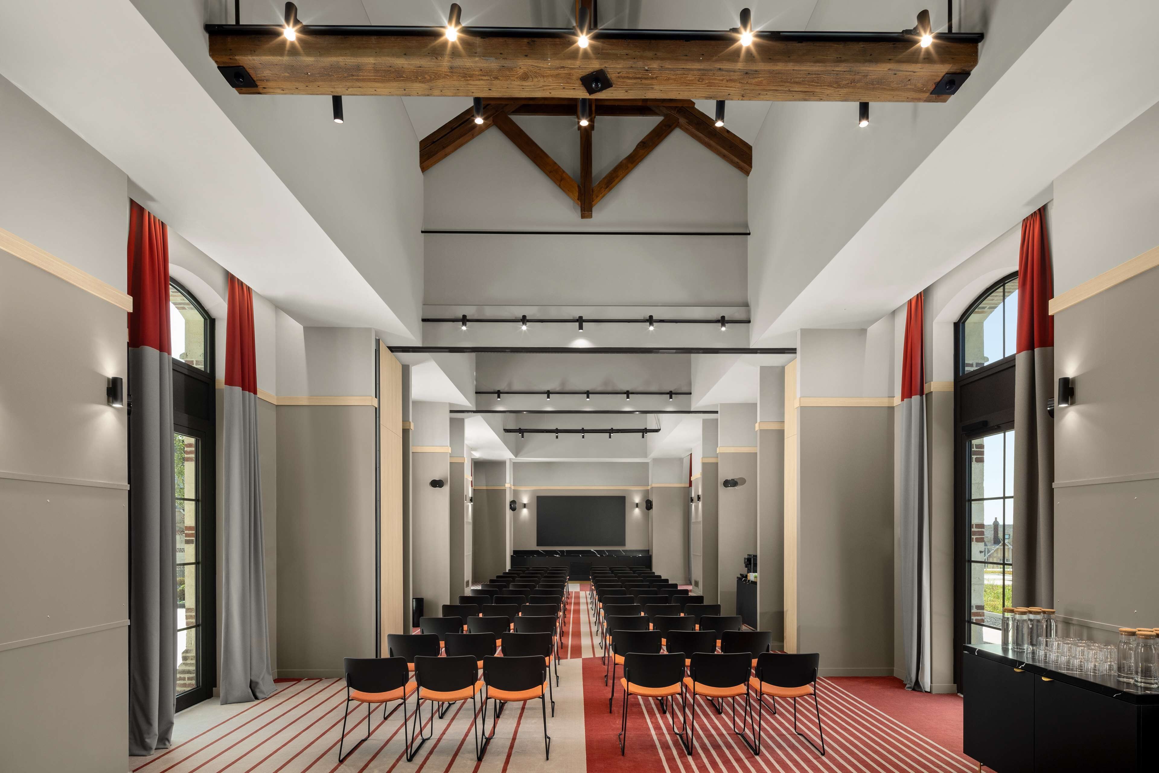 A conference room with rows of chairs, a large screen, and a wooden ceiling structure.