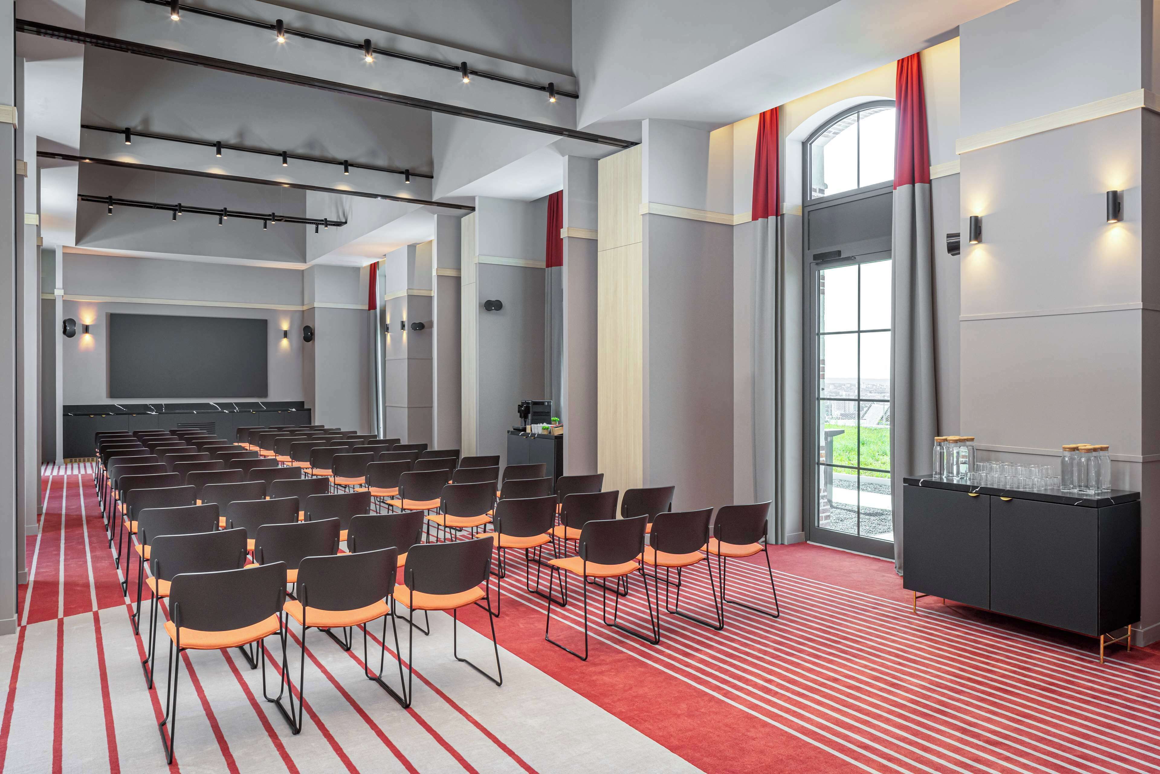 A conference room with rows of chairs, a black cabinet with glass containers, and a red carpet.