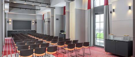 A conference room with rows of chairs, a black cabinet with glass containers, and a red carpet.