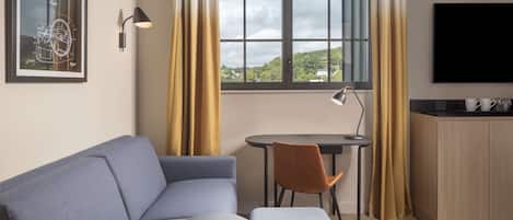 A modern room with a sofa, a small table, a chair, a TV, and a window with curtains.