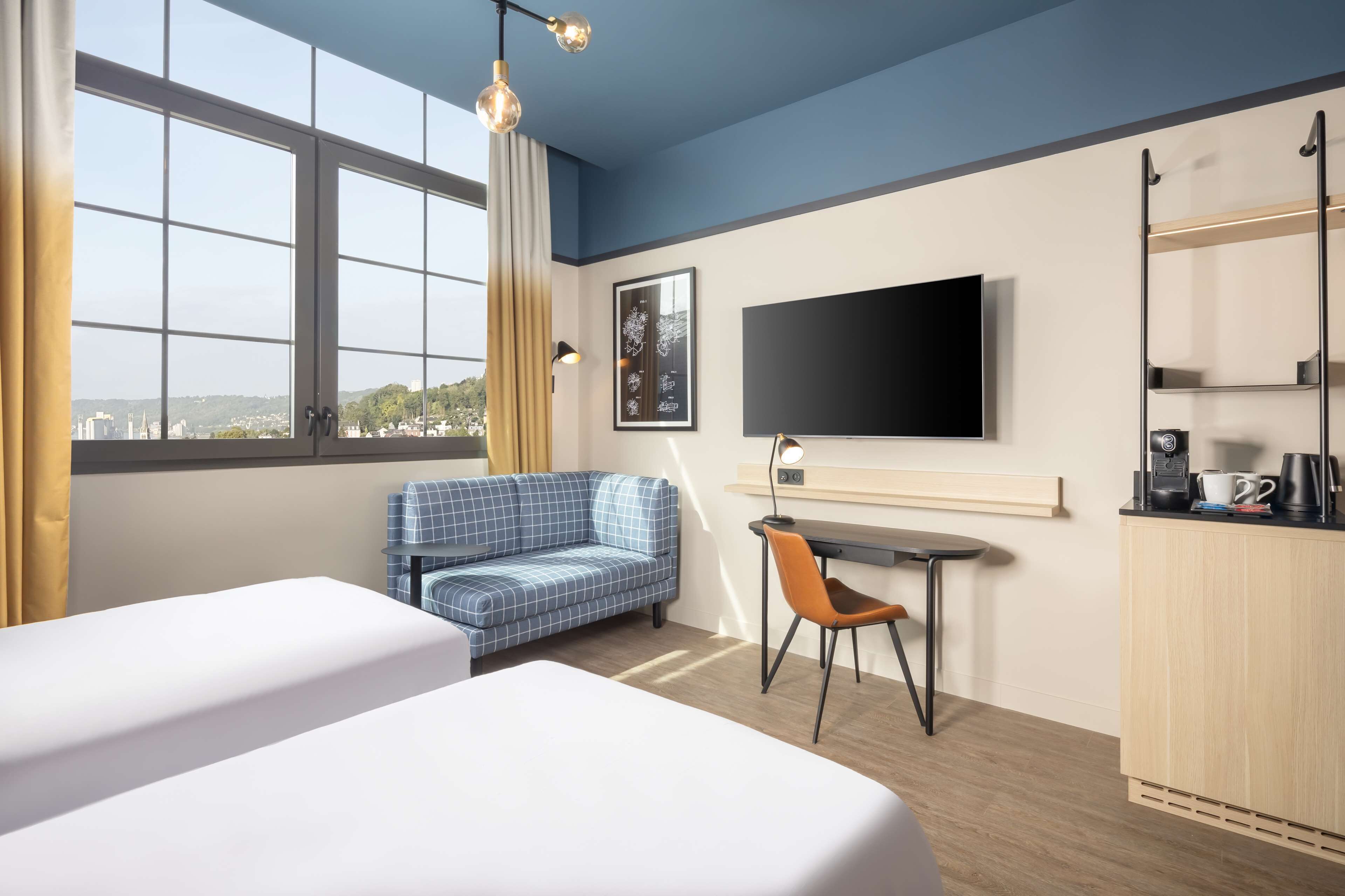 A hotel room with two beds, a desk with a chair, a TV, and a city view.