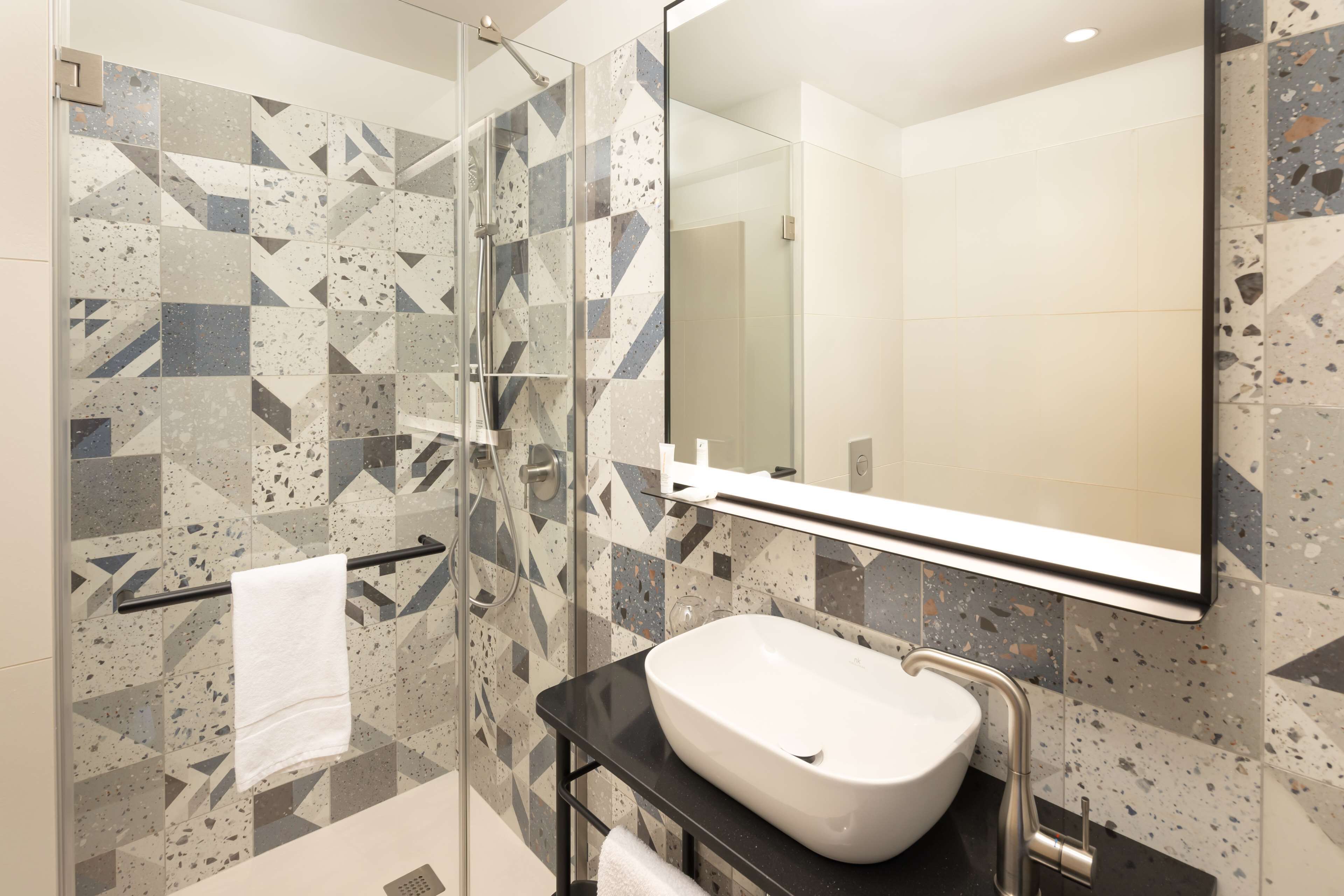 A modern bathroom with a glass shower enclosure, a white sink, and a large mirror.