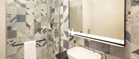 A modern bathroom with a glass shower enclosure, a white sink, and a large mirror.