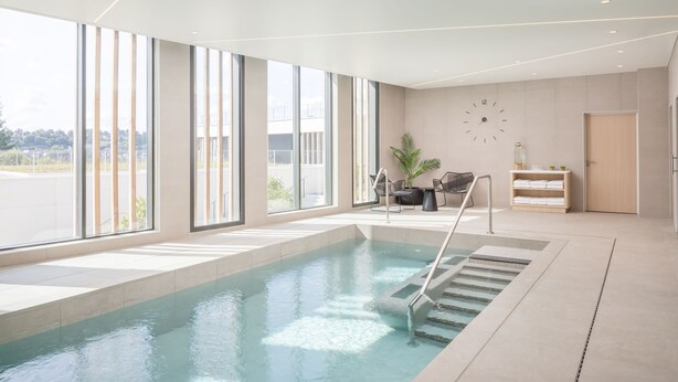 A modern indoor swimming pool with large windows, a clock, and a seating area with a plant. - Hyatt Place Rouen (Rouen)