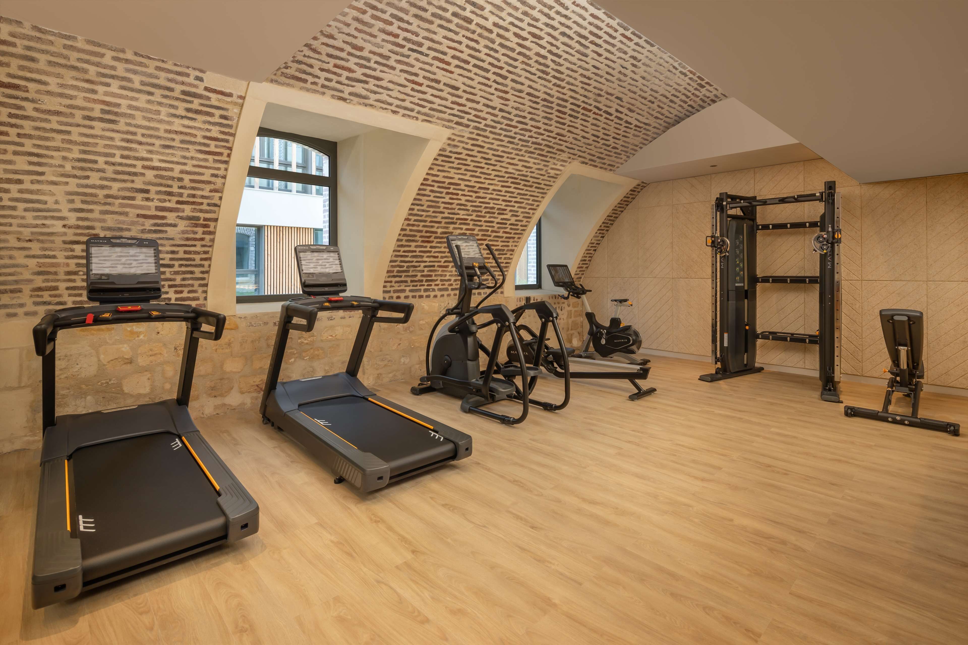 Une salle de sport équipée de tapis de course, de vélos elliptiques et d'un espace dédié à la musculation.