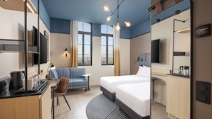 A hotel room with a bed, a desk with a kettle, a chair, a sofa, a TV, a mirror, and a view of the city through large windows. - Hyatt Place Rouen (Rouen)