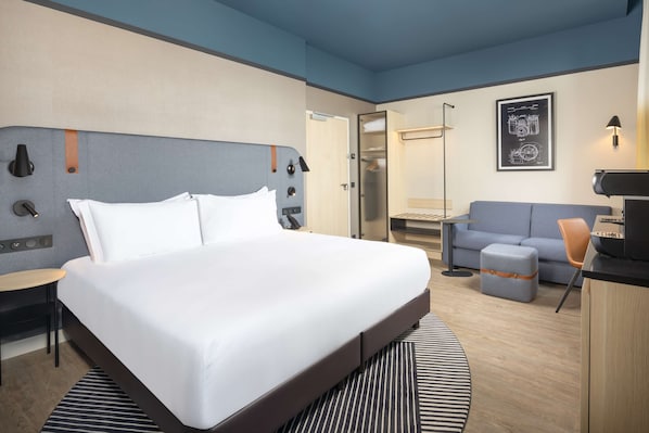 Una habitación de hotel moderna con una cama grande, un escritorio, un sofá y un armario.