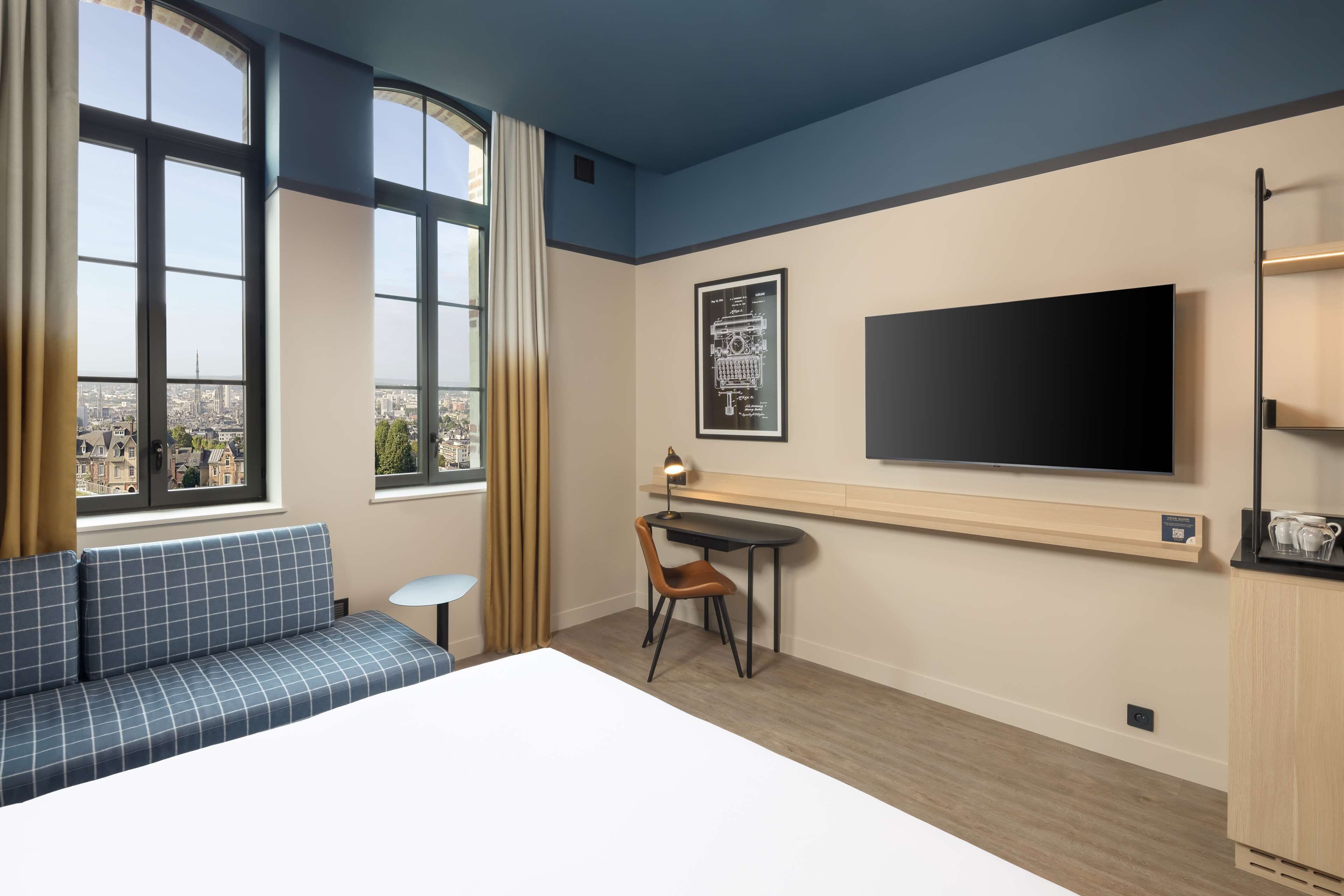 Quarto de hotel moderno com uma cama grande, uma escrivaninha com cadeira, televisão e sofá.