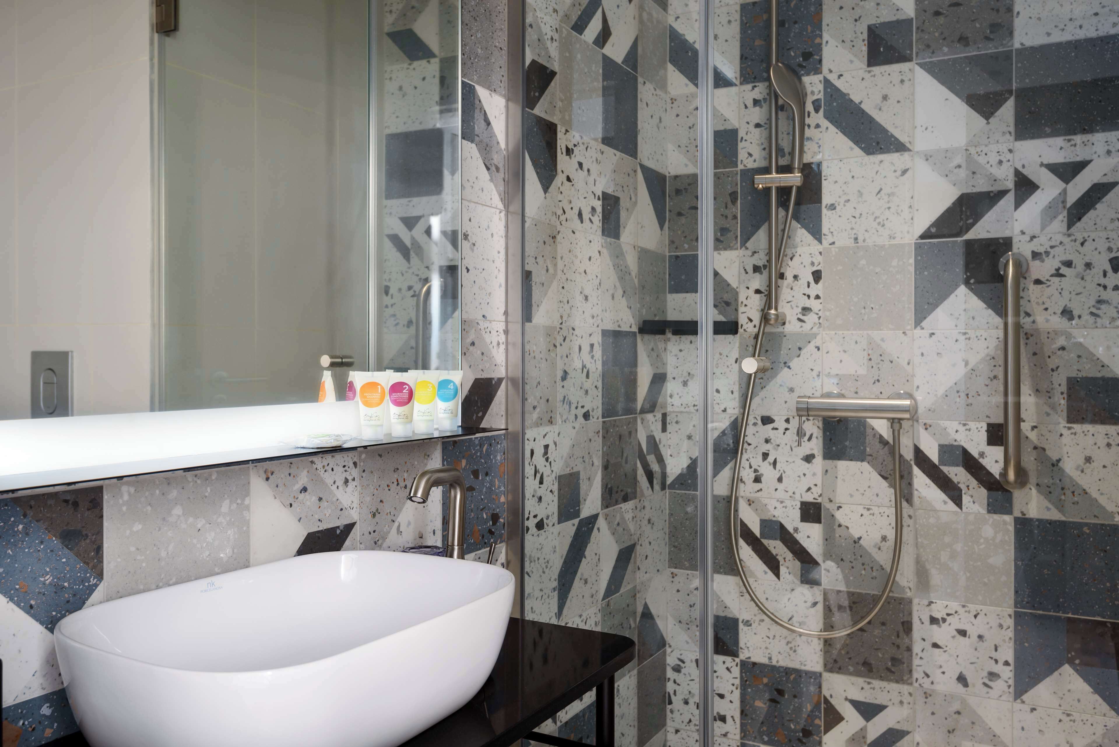 A bathroom with a white sink, a glass shower enclosure, and a tiled wall with geometric patterns.